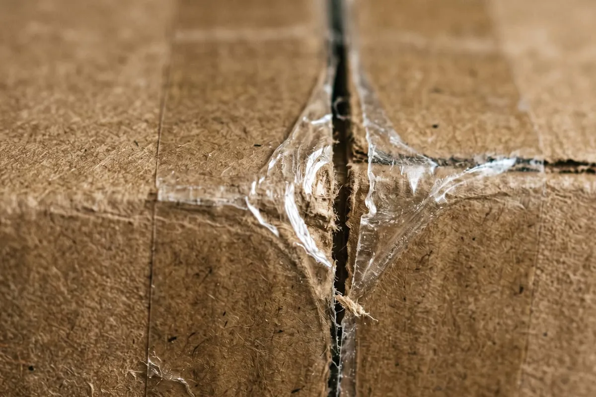 Close da emenda de uma caixa de papelão em que a fita foi cortada e pressionada de volta, com a borda deslocada aparecendo na luz